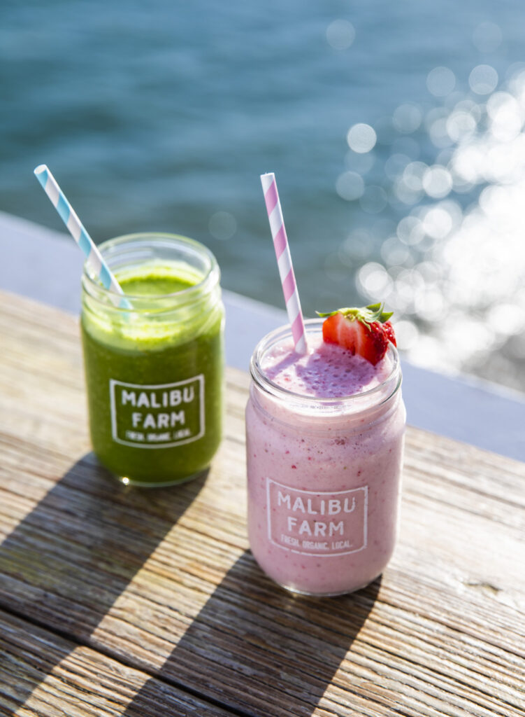 Two smoothies on a wooden railing located by the San Diego bay. One strawberry and one made of greens