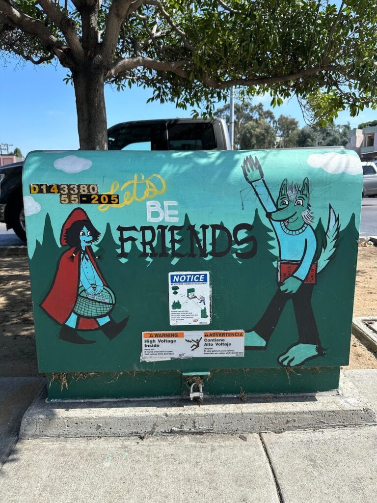A Point Loma utility box mural with little red riding hood and the big band wolf waving at each other with the text "Let's Be Friends" enscribed